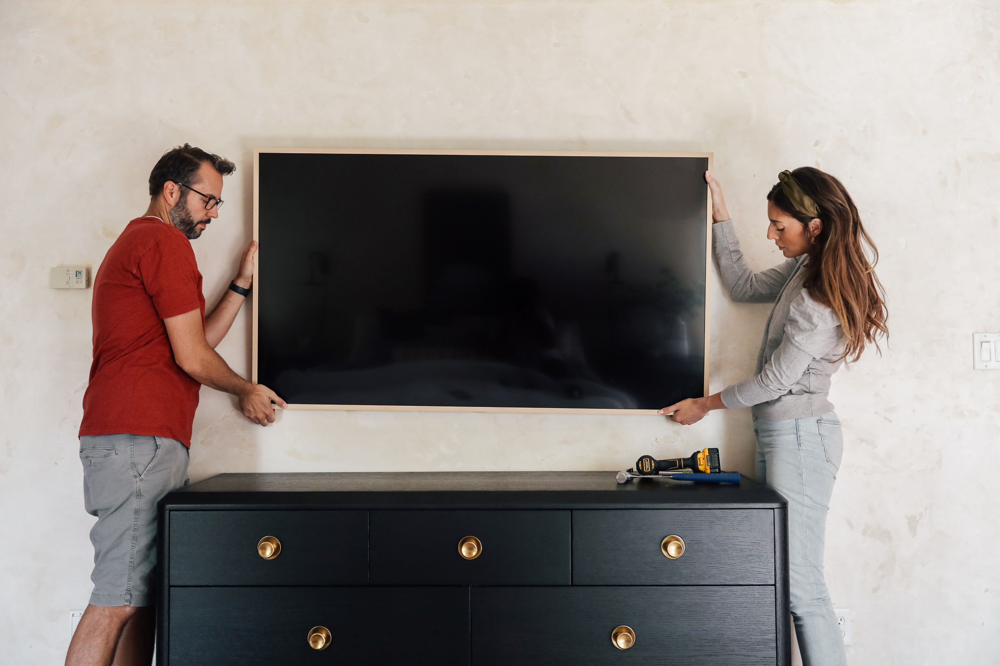Chris & Julia hanging a Samsung Frame TV on a cream wall above a black dresser.