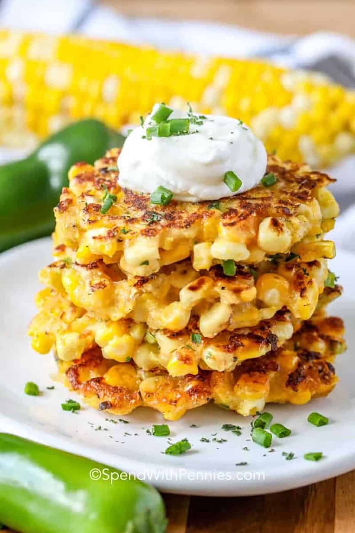 Corn fritters are a crispy fried side dish or appetizer that have layers of satisfying flavor in every bite. Corn meal and kernels are mixed up in a boldly seasoned batter with shredded cheese, jalapenos and smoked paprika, then fried to a golden brown. This easy recipe is quick to prep and cook. Make it richer with cream, or add extra nutrition with shredded zucchini or sweet potatoes. Serve with sour cream or hot sauce. It’s an easy way to add a pop of flavor to any meal. #spendwithpennies stack of Corn Fritters