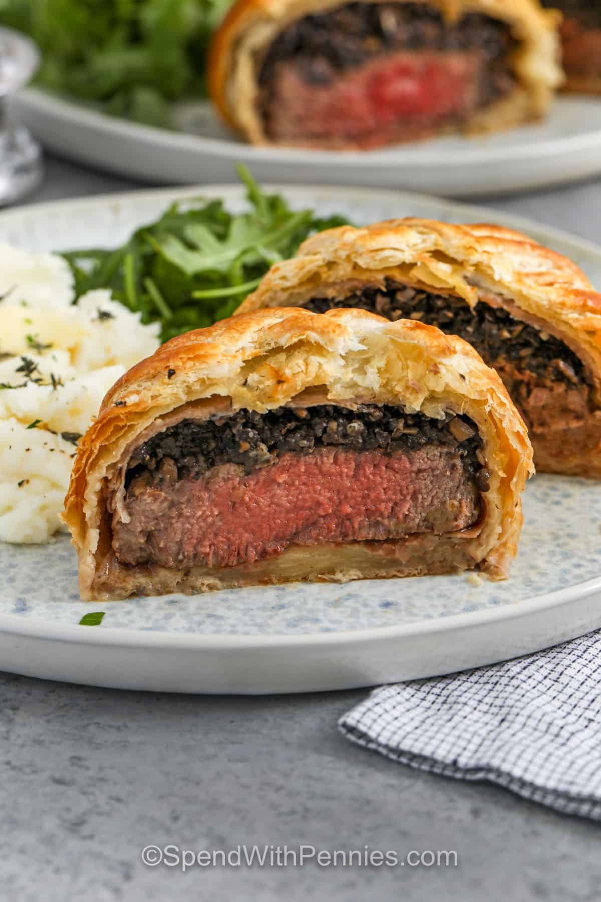 A flaky crust, juicy filet mignon, and garlicky mushrooms make this Beef Wellington recipe a dinner to remember. It’s one of those showstopper meals that turns out beautiful every time with a few easy steps. The prosciutto adds a salty bite that pairs perfectly with the rich filling, and that Dijon mustard gives it the perfect little zing. It's special enough for guests, but easy enough for anytime! #spendwithpennies close up of Beef Wellington cut in half