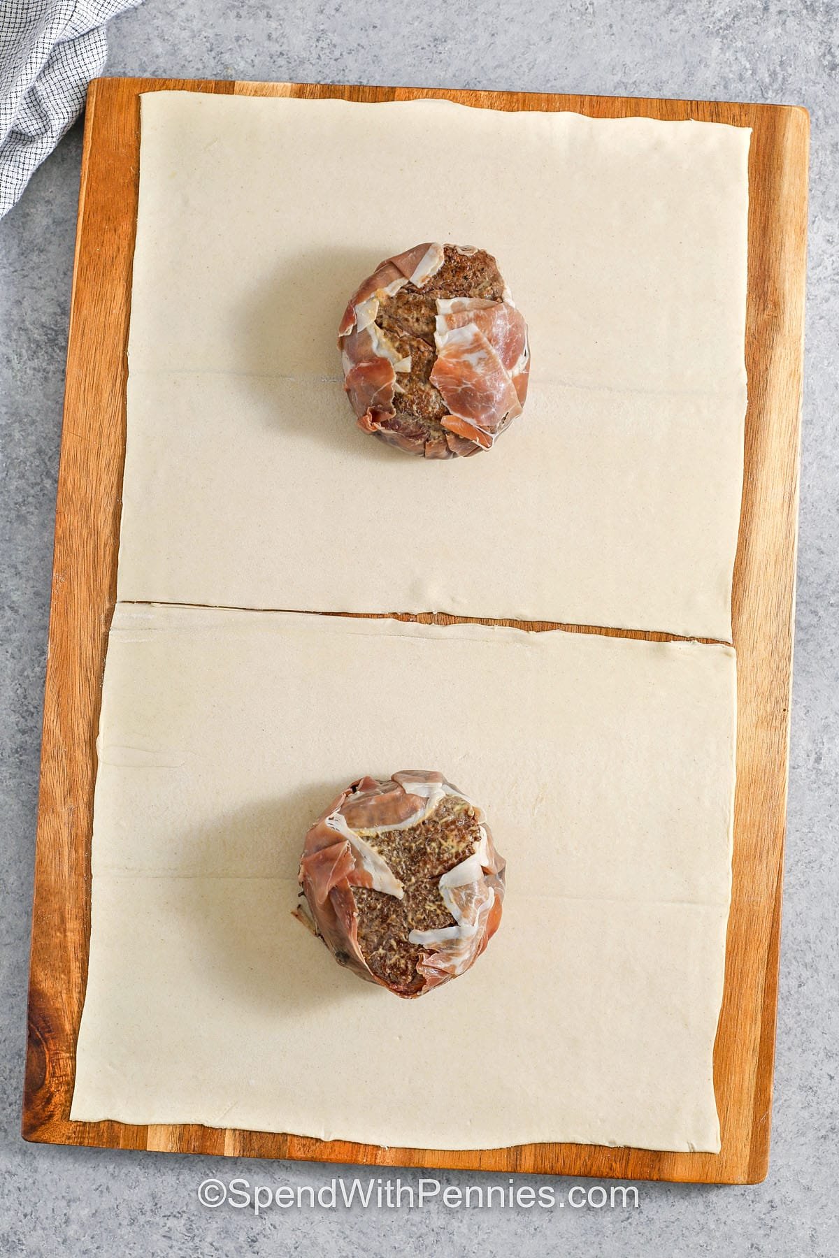 This Beef Wellington recipe wraps tender filet mignon in a layer of savory mushrooms, salty prosciutto, and golden, flaky puff pastry. Every bite is buttery, juicy, and full of rich flavor that feels like a restaurant meal made right at home. It's a beautiful way to impress guests or just treat yourself to something special without the fuss. Don't forget the mushroom duxelles—it makes all the difference! #spendwithpennies adding beef and prosciutto to puff pastry to make Beef Wellington