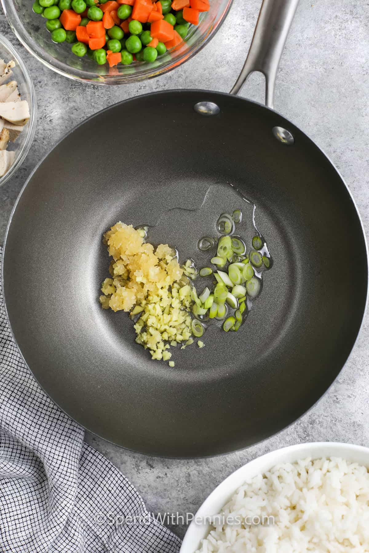 Chicken fried rice is one of those recipes you’ll turn to again and again. It’s quick, tasty, and made with pantry staples like frozen veggies and soy sauce. A little garlic, ginger, and toasted sesame oil bring tons of flavor. Great as a main or a side, and perfect for lunch the next day too! Leftovers never looked so good. #spendwithpennies oil with garlic , ginger and green onions cooking in a pan to make Easy Fried Rice Recipe