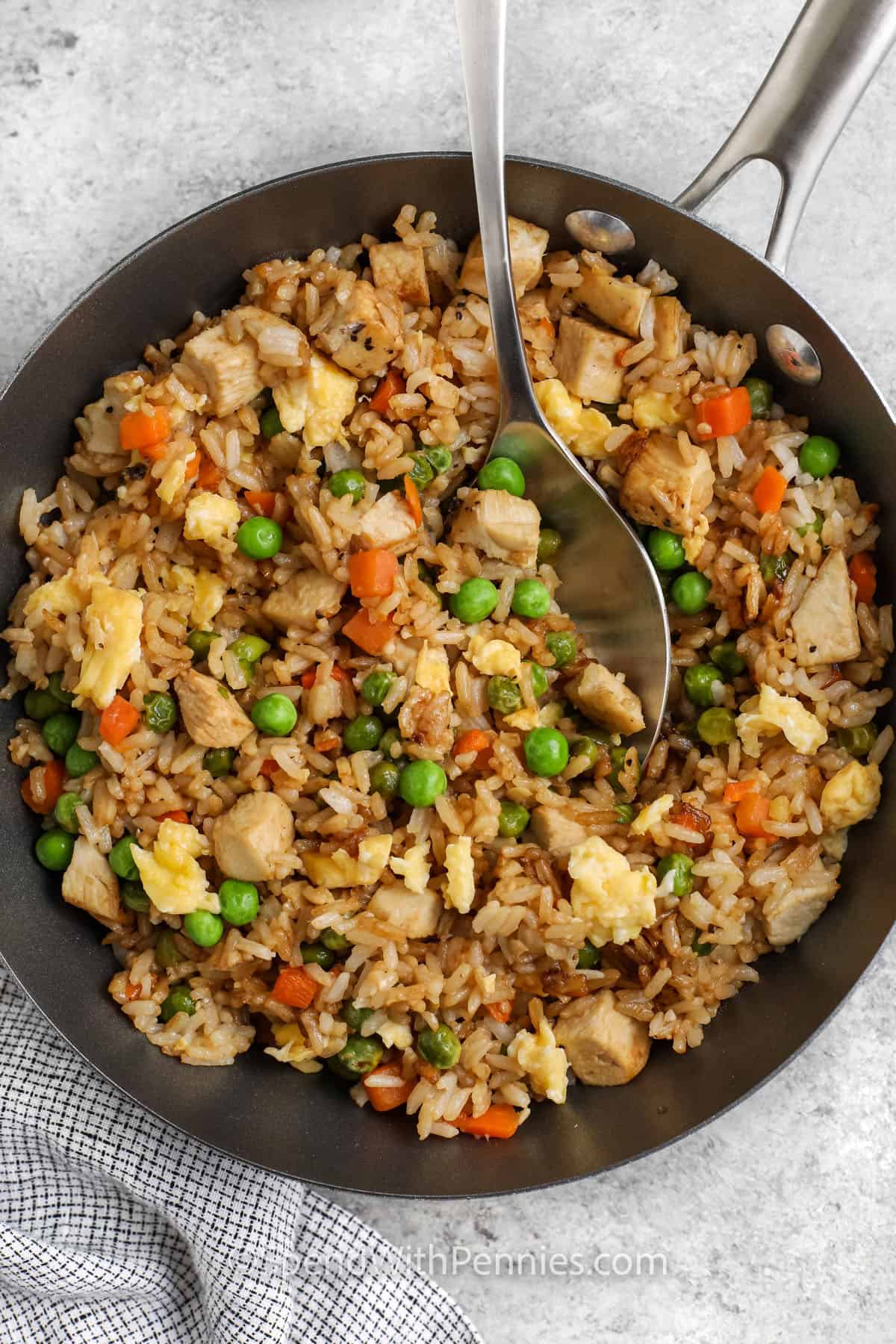 Chicken fried rice is a one-pan wonder filled with colorful veggies, scrambled egg, and tender chicken. It’s made with day-old rice for that perfect fried texture and finished with toasted sesame oil. You can customize it with whatever you’ve got in your fridge. Simple and oh-so-good! #spendwithpennies Easy Fried Rice Recipe in a pan with a spoon