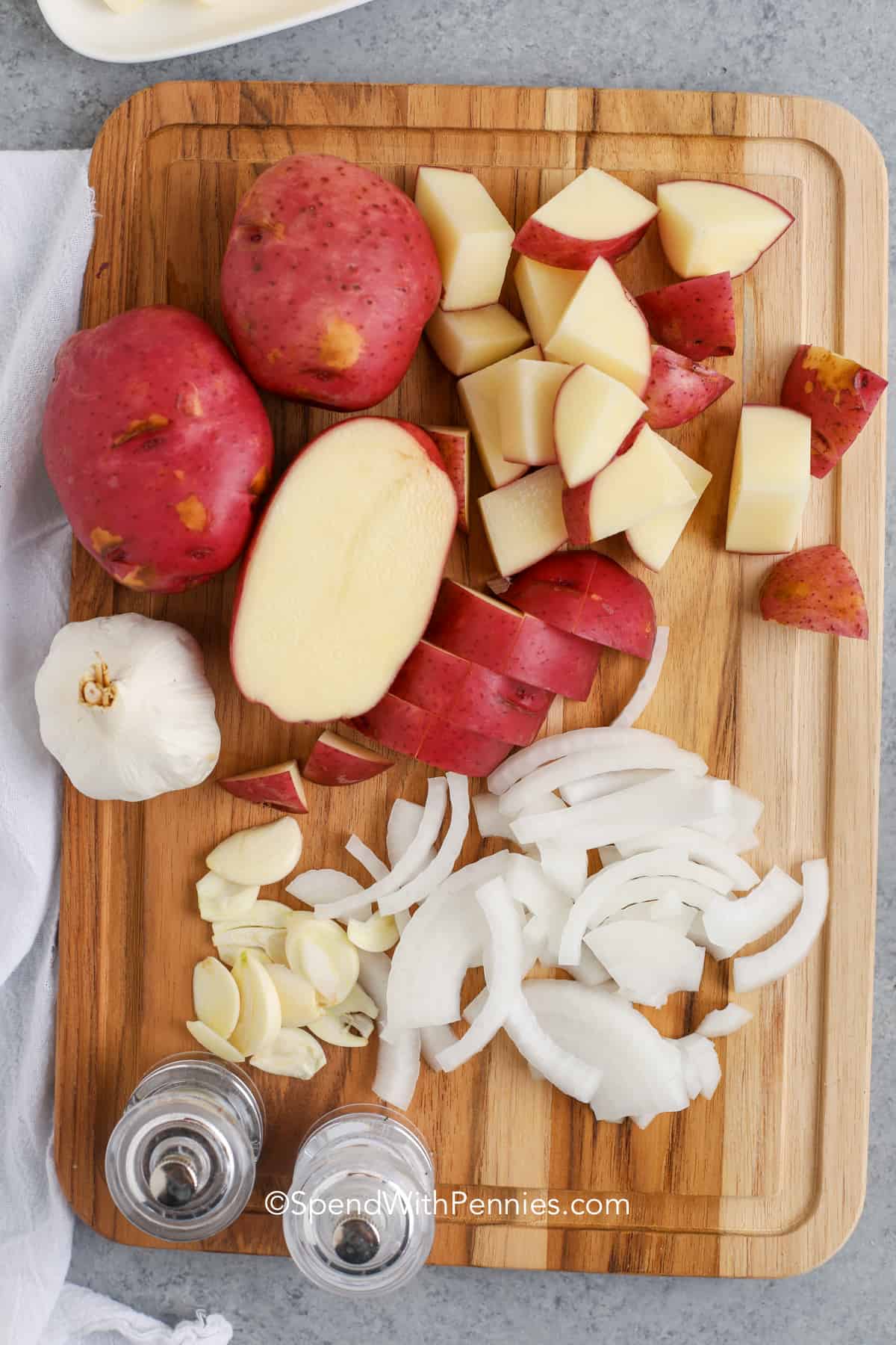 Grilled potatoes bring all the flavor with hardly any cleanup! Just season red potatoes with butter, garlic, rosemary, and onions, wrap them in foil, and let the grill do the work. They’re golden on the outside and soft on the inside, perfect with anything from grilled chicken to juicy burgers. So easy and so delicious! #spendwithpennies Grilled Red Potatoes ingredients on a cutting board