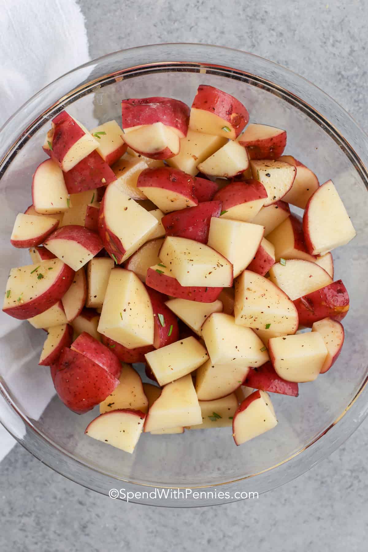 Grilled potatoes are a must when you’re firing up the grill! Red potatoes and onions soak up buttery garlic and rosemary flavor, then roast to perfection in a foil packet. They’re soft inside, crisp on the edges, and taste amazing with sour cream or ranch. You’ll want to make extras—these go fast at any BBQ! #spendwithpennies potatoes with seasonings in a bowl to make Grilled Red Potatoes