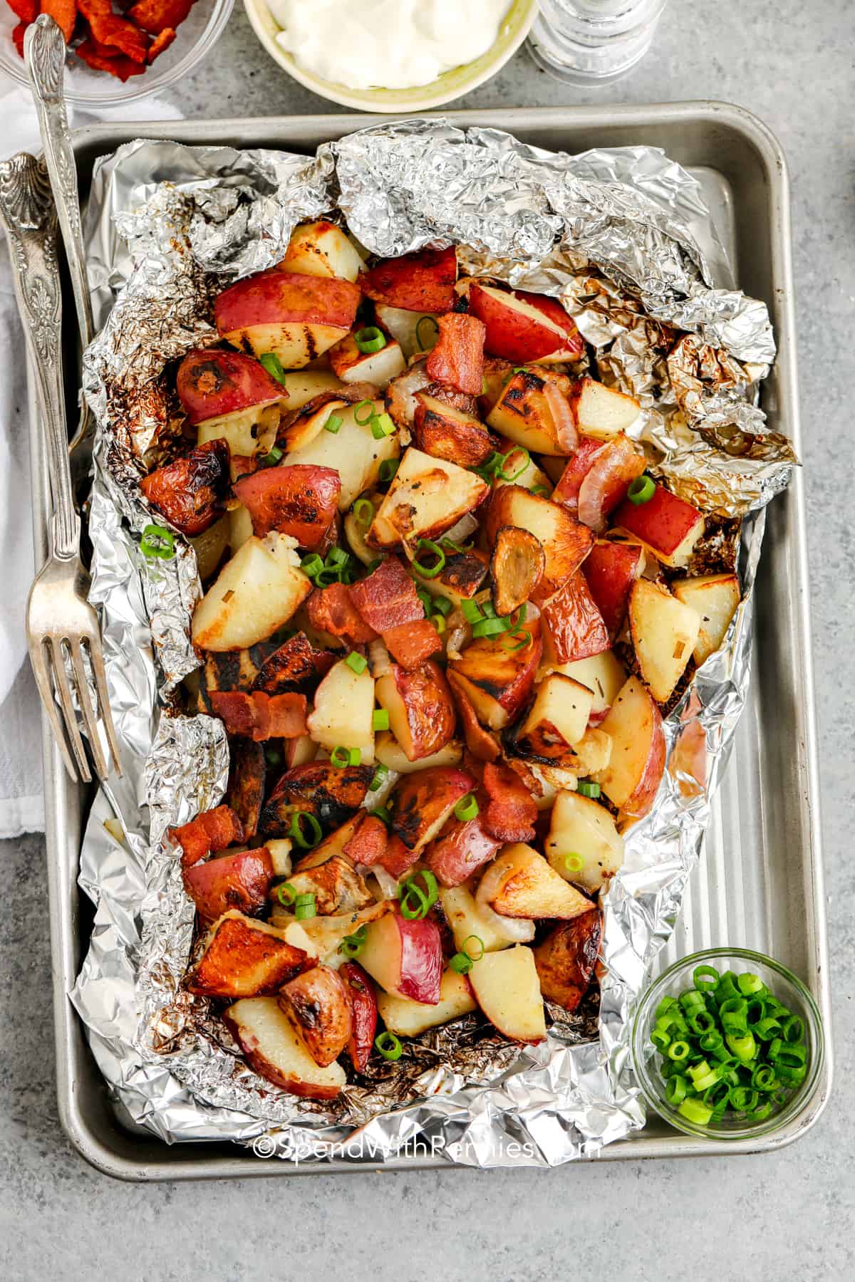 Grilled potatoes bring buttery goodness to your plate with every bite! Wrapped in foil with garlic, rosemary, and onions, they turn golden and delicious right on the grill. Great for a weeknight dinner or weekend barbecue, this easy side will quickly become a favorite. Try them with your go-to grilled mains! #spendwithpennies Grilled Red Potatoes on a sheet pan with green onions