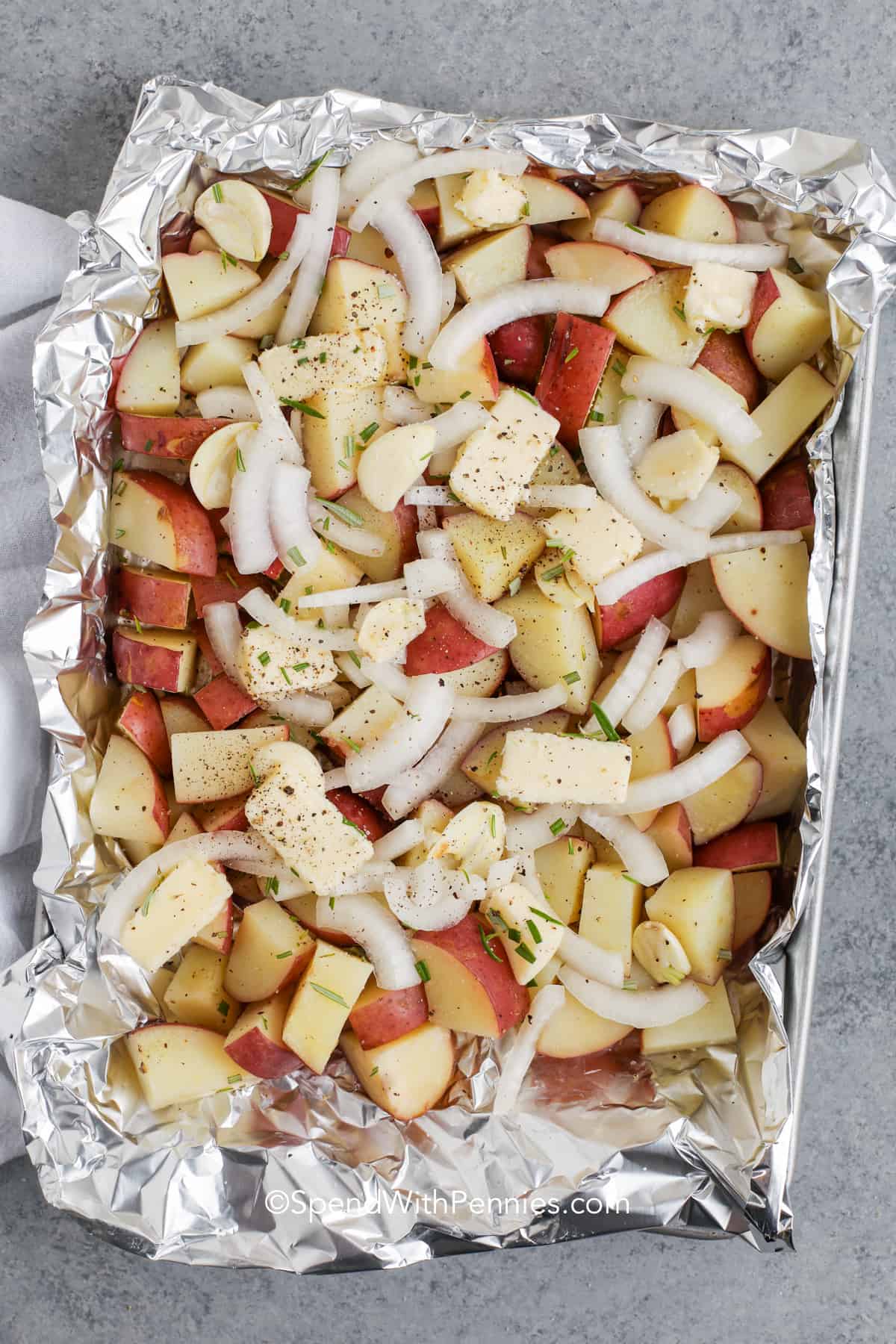 Grilled potatoes cook up tender with crispy edges and so much flavor! Tossed with garlic, onions, rosemary, and butter, these foil packet potatoes are a backyard BBQ favorite. They’re cozy enough for fall but light and fresh for summer. Perfect next to a juicy burger or grilled chicken breast! #spendwithpennies adding butter onions and salt and pepper to potatoes to make Grilled Red Potatoes
