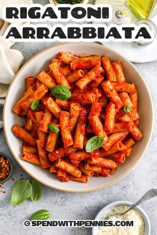 Rigatoni Arrabbiata is a spicy, bold pasta dish that’s easy to whip up with pantry ingredients! Crushed tomatoes, red chili flakes, and garlic bring heat and flavor, while rigatoni soaks up every saucy bite. Perfect for weeknights or when cravings strike, it’s ready in about 30 minutes. A sprinkle of parmesan and fresh herbs takes it over the top! #spendwithpennies plated Rigatoni Arrabbiata with a title
