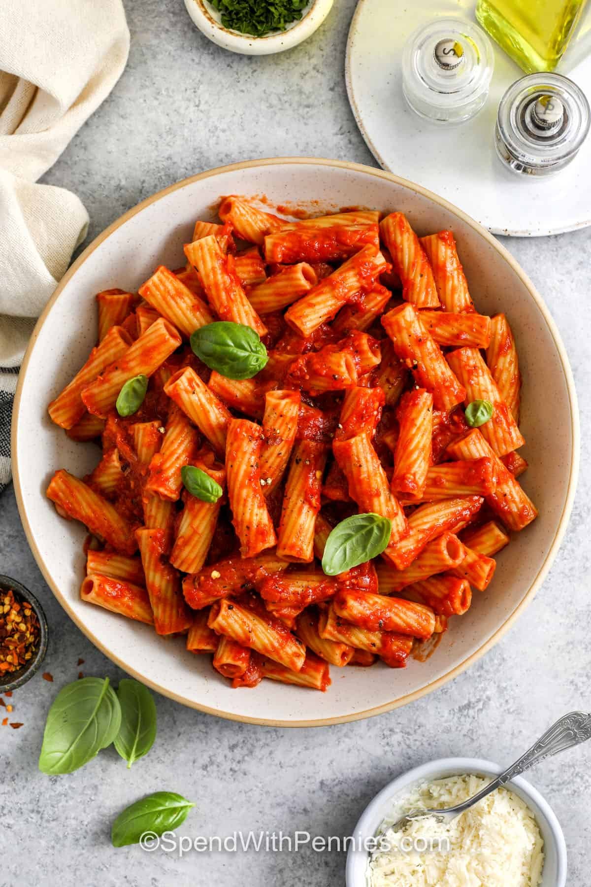 Rigatoni Arrabbiata is a simple yet spicy Italian pasta that brings a kick of heat to the dinner table. With red chili flakes, garlic, and basil simmered in crushed tomatoes, every bite is full of bold flavor. Rigatoni holds the rich sauce perfectly, making it extra satisfying. Finish with a drizzle of olive oil and cheese for a restaurant-style touch! #spendwithpennies top view of rigatoni arrabbiata in a white serving bowl with parmesan
