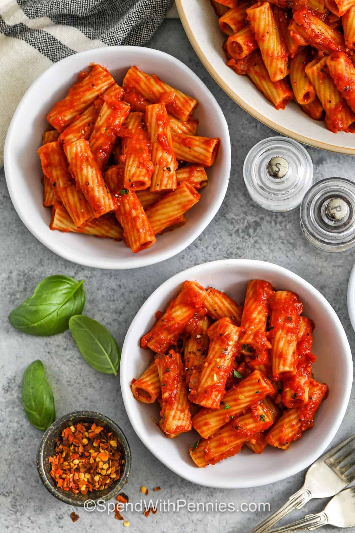 Rigatoni Arrabbiata brings the heat with red chili flakes and garlic in a vibrant tomato sauce. This classic Italian dish is fast, flavorful, and budget-friendly! Rigatoni’s shape grabs all that spicy, saucy goodness. Perfect for meatless Mondays or anytime you want a punch of flavor in your recipe. #spendwithpennies rigatoni arrabbiata in a individual serving bowls with chili flakes