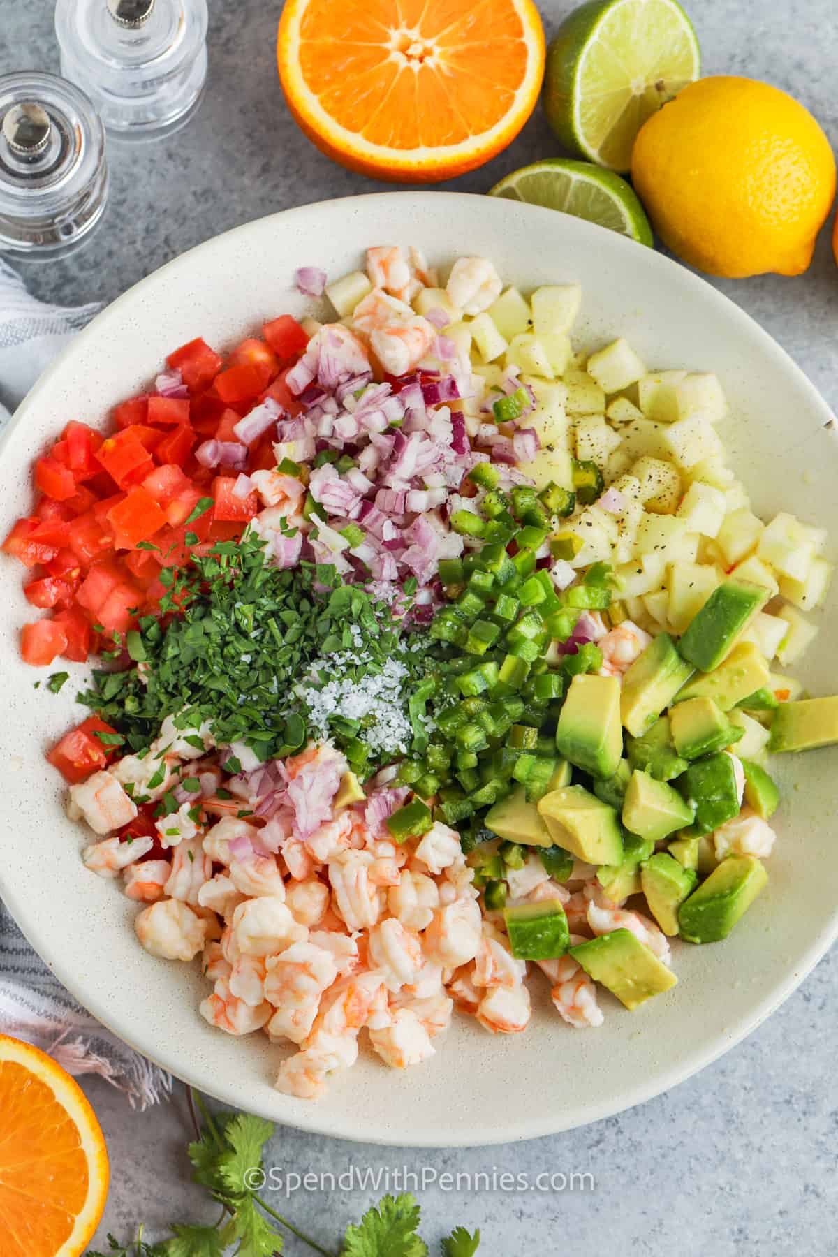 Make the tastes of Mexico with this shrimp ceviche recipe. This easy no-cook salad is ready in minutes with no cooking required. Healthy and low in calories, this shrimp ceviche is sure to please everyone. Made with tomatoes, jicama, peppers, cilantro, and onions, and topped with some avocado, this salad is colorful, flavorful, and crunchy! #spendwithpennies ingredients in a bowl to make Shrimp Ceviche