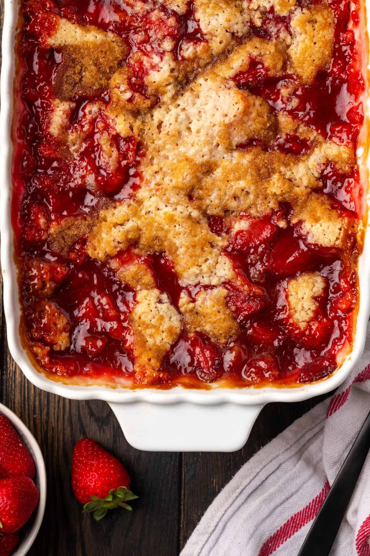 Overhead view of a baked strawberry cobbler in a ceramic baking dish.