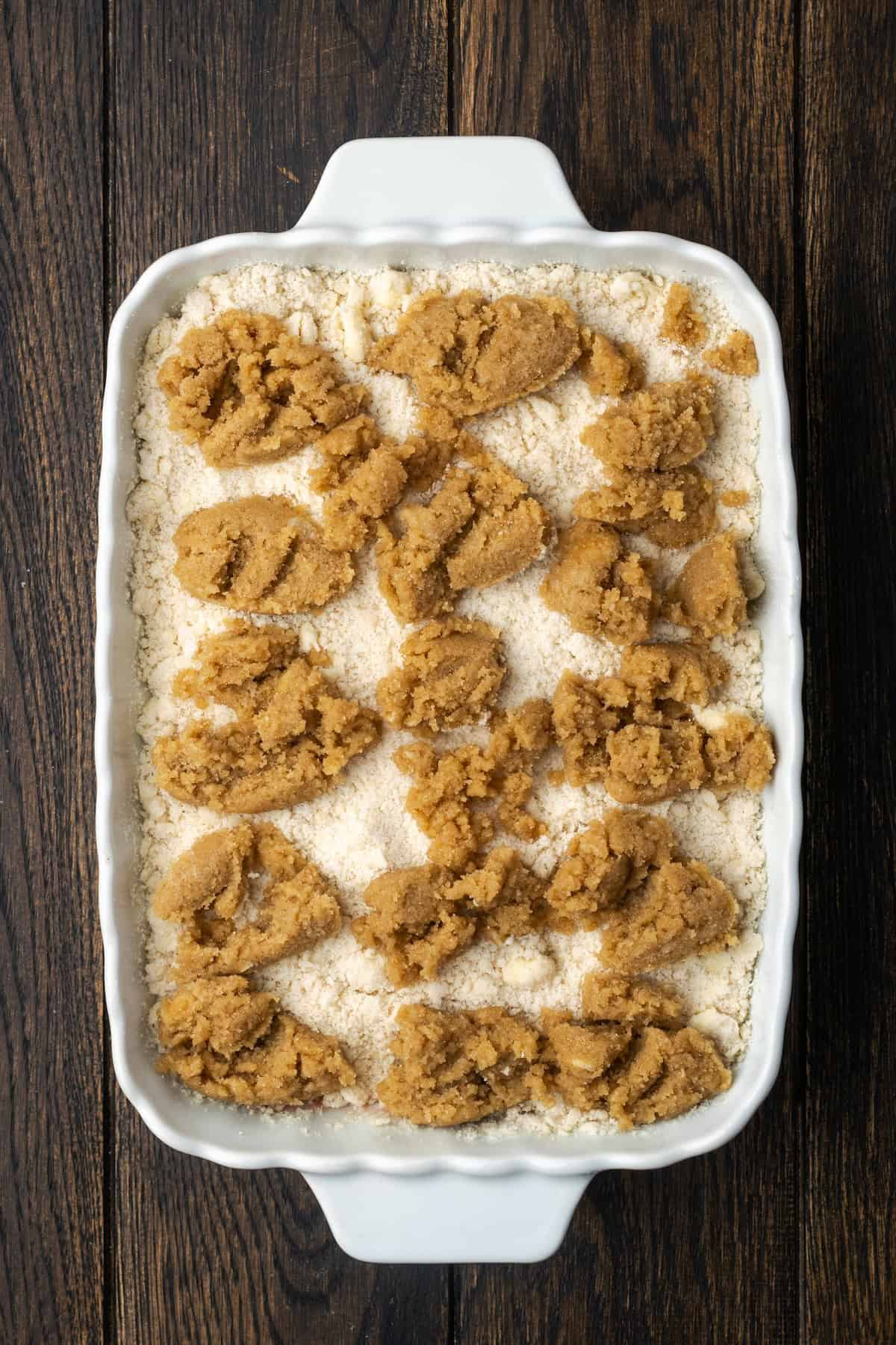 Brown sugar-butter mixture dolloped over the crumble topping of a strawberry cobbler in a baking dish.