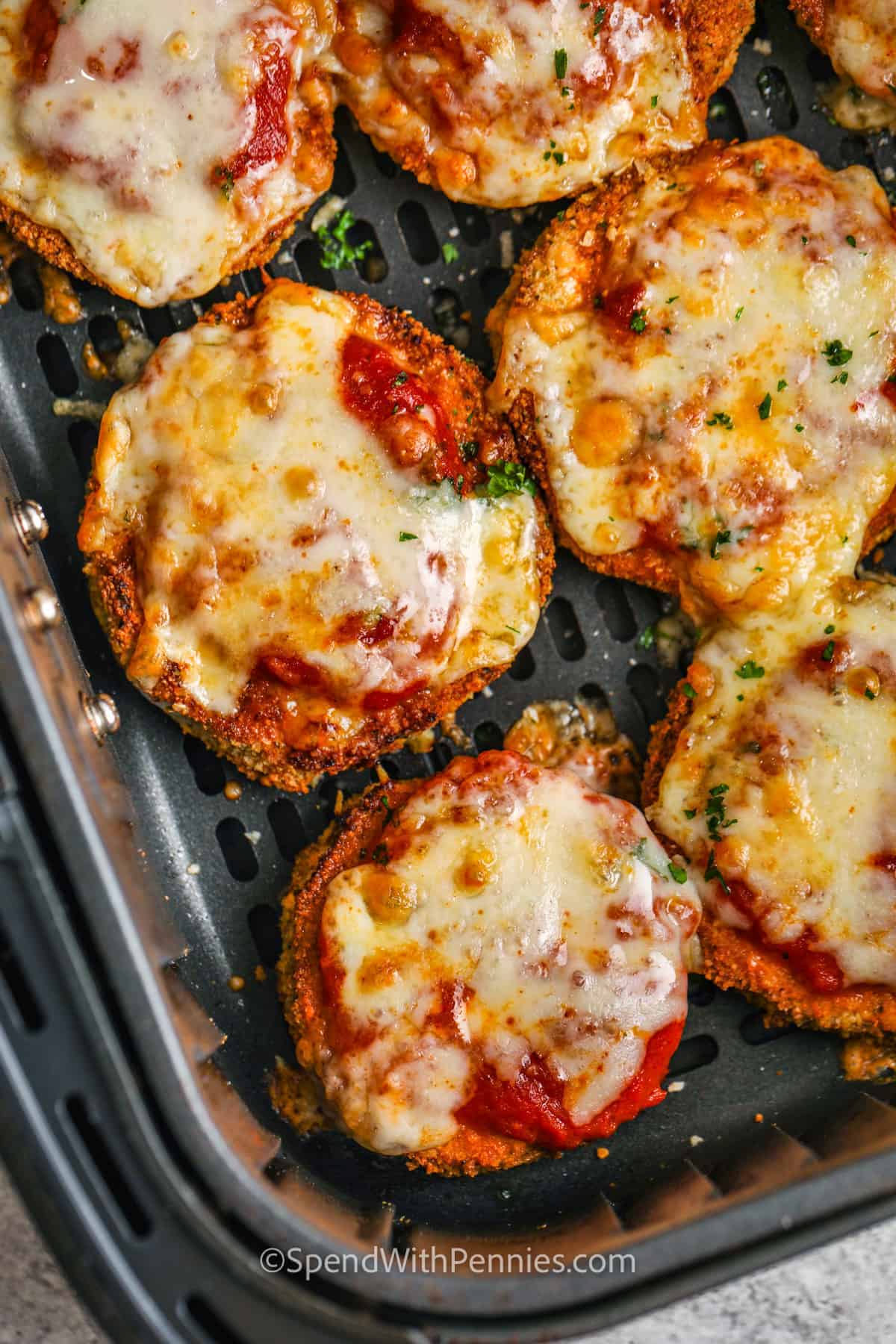If you're craving comfort food, this air fryer eggplant parmesan is the best way to get it! Slices of eggplant are breaded and air fried until crispy and golden, then topped with sauce and cheese and cooked until bubbly. Try it with chicken for a heartier twist, or skip the crumbs for a keto version. It's an easy recipe you'll want to make again and again! #spendwithpennies close up of cooked Air Fryer Eggplant Parmesan