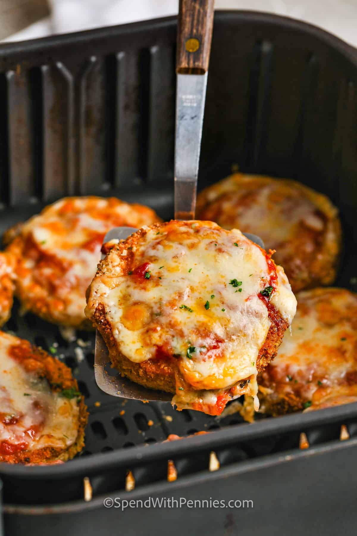If you're looking for the best way to make eggplant parmesan, this air fryer eggplant parmesan recipe is it! The slices get breaded, then fried up in the air fryer until they’re golden and crispy. Top with sauce and cheese, and cook just until bubbly. Try it with chicken for a hearty version or go keto by skipping the breadcrumbs. It’s an easy weeknight favorite with all the comfort you love. #spendwithpennies taking Air Fryer Eggplant Parmesan out of the fryer