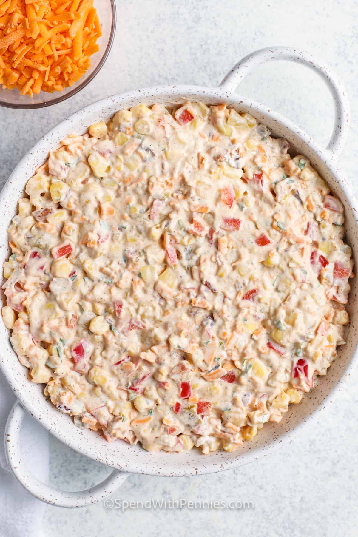 Corn dip is a creamy, cheesy recipe with bold street-style flavors that always disappears fast at parties. Made with sweet corn, chiles, chili powder, cheddar, and sour cream, it bakes up hot and bubbly every time. Scoop it with tortilla chips or serve it cold for a quick version. Add black beans for a meatless dip, or mix in seasoned beef to make it extra hearty and satisfying! #spendwithpennies Creamy Baked Corn Dip in the dish before adding cheese
