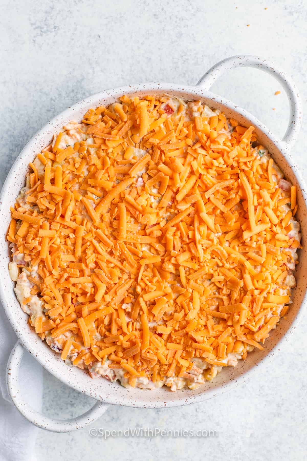 This corn dip recipe is cheesy, creamy, and full of flavor with a little kick from chiles and chili powder. It’s inspired by the bold tastes of Mexico and bakes up hot and bubbly for the perfect party snack. Serve it with your favorite chips, or chill it for a quick cold dip. Add ground beef for a heartier version, or toss in black beans to keep it vegetarian and filling. #spendwithpennies adding cheese to dish to make Creamy Baked Corn Dip