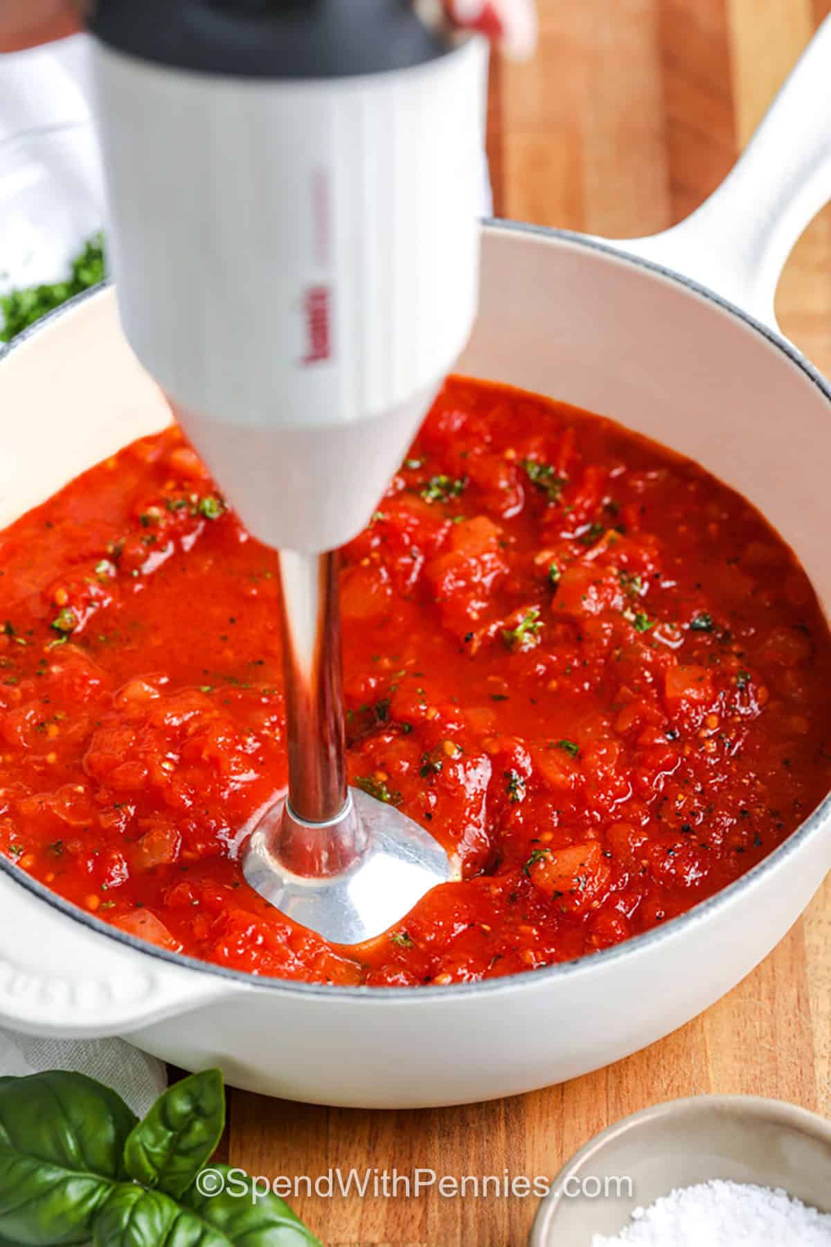 Tomato sauce is easy to make and packed with rich, natural flavor from whole tomatoes and aromatic herbs. A quick simmer brings the sauce together, and blending is optional depending on your desired texture. Use this sauce on pasta, pizza, or even with creamy chicken dishes. It’s fresh, fast, and far better than store-bought! #spendwithpennies blending ingredients in pot to make Tomato Sauce